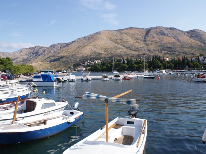Colorful small boats docked along the Cavtat harbor with mountains rising behind the coastal town