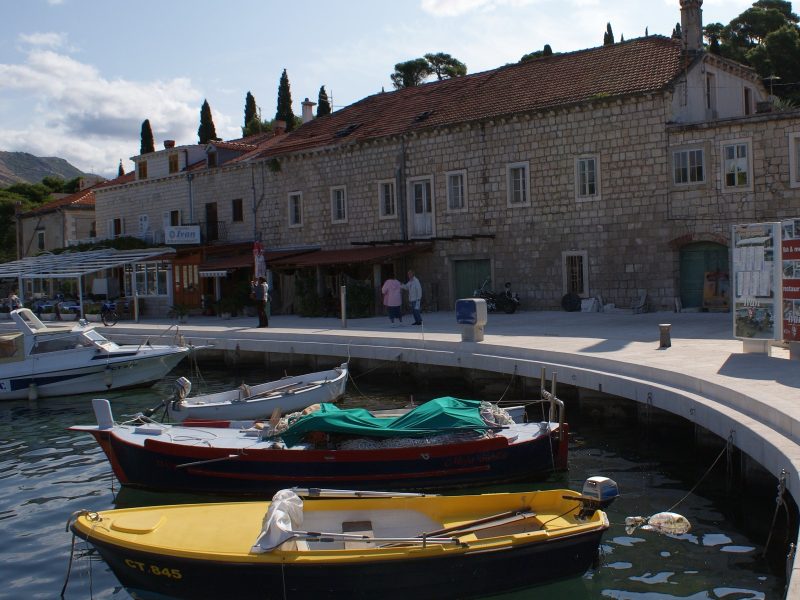 Waterfront promenade in Cavtat lined with stone buildings, palm trees, and moored boats along a curving harbor