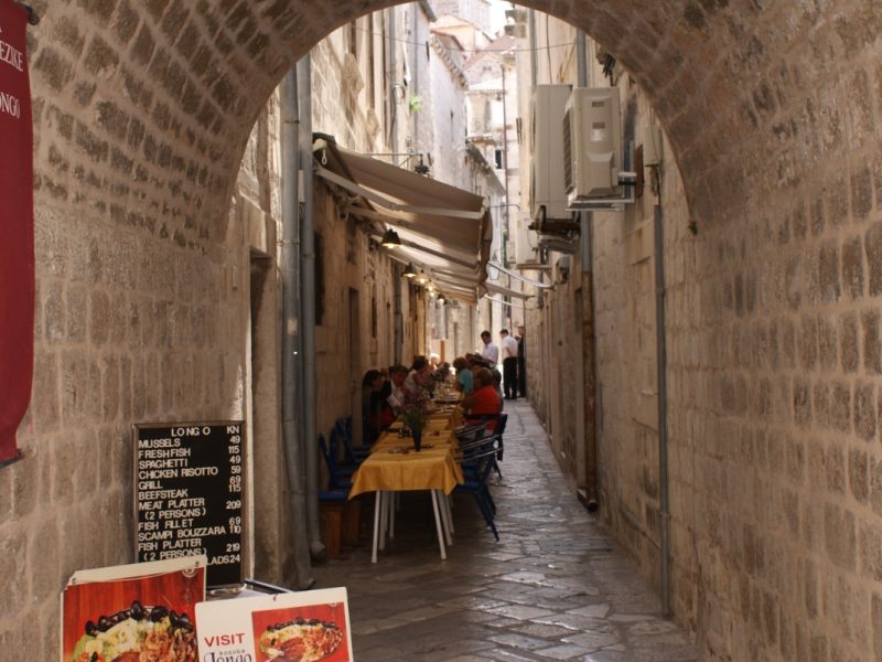 Narrow stone alley in Dubrovnik's Old Town with an arched stairway and a restaurant sign