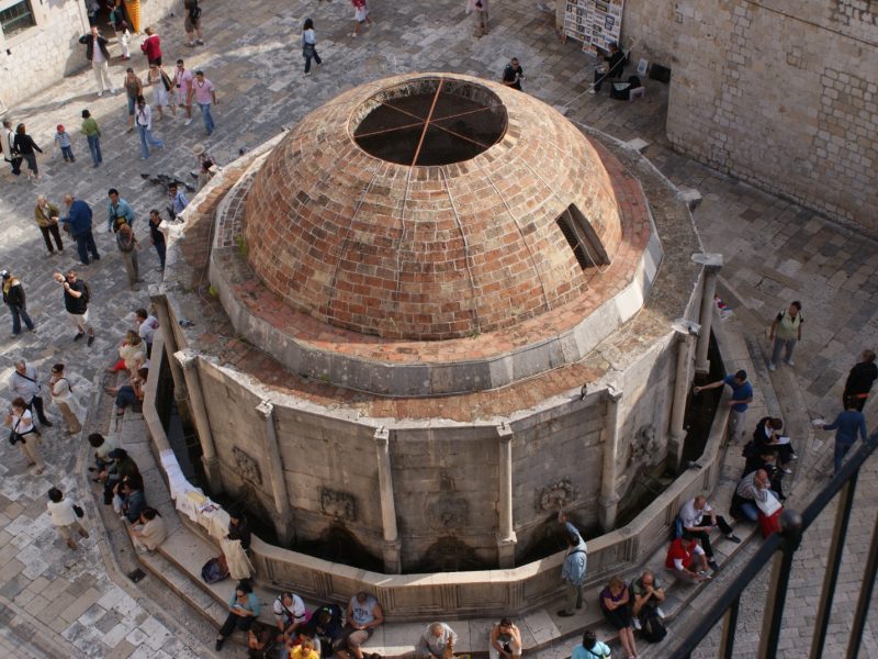 Aerial view of Onofrio's Fountain's domed roof in Dubrovnik's Old Town, with tourists gathered in the surrounding stone square