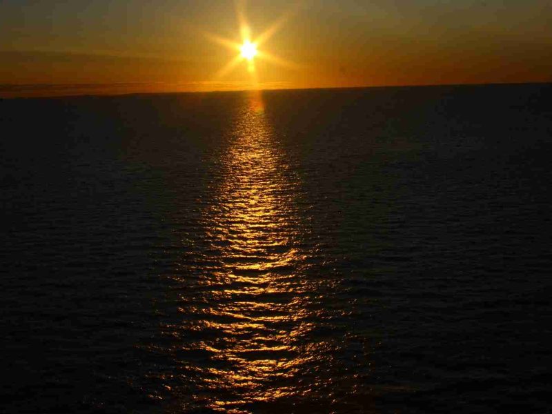 Sun setting over the ocean with a golden reflection path across the water