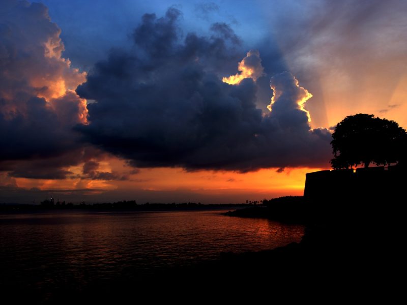 Silhouette of a coastal fortress and tree against a dramatic orange sunset over the water